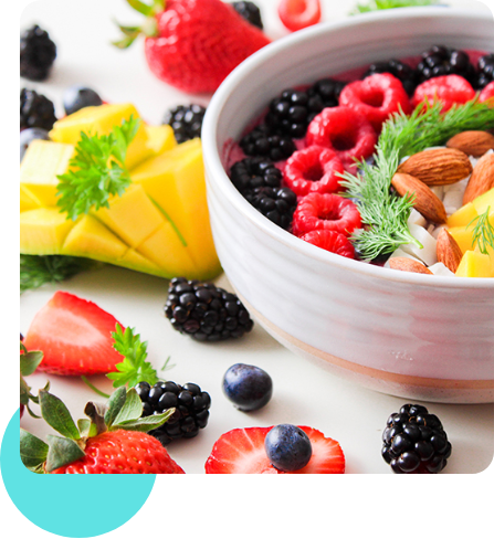 Eine Schale gefüllt mit frischen Beeren, Mandelkernen und weiteren Früchten. Um die Schale liegen weitere Früchte und Beeren.