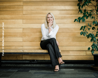 Dr. Mareike Streker; junge blonde Frau sitzt vor einer Holzwand