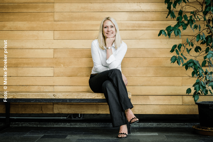 Dr. Mareike Streker; junge blonde Frau sitzt vor einer Holzwand