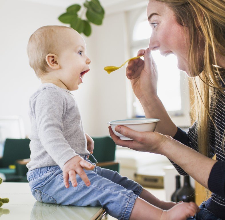 Eine lächelnde Mutter, die ihr kleines Kind mit Brei füttert.