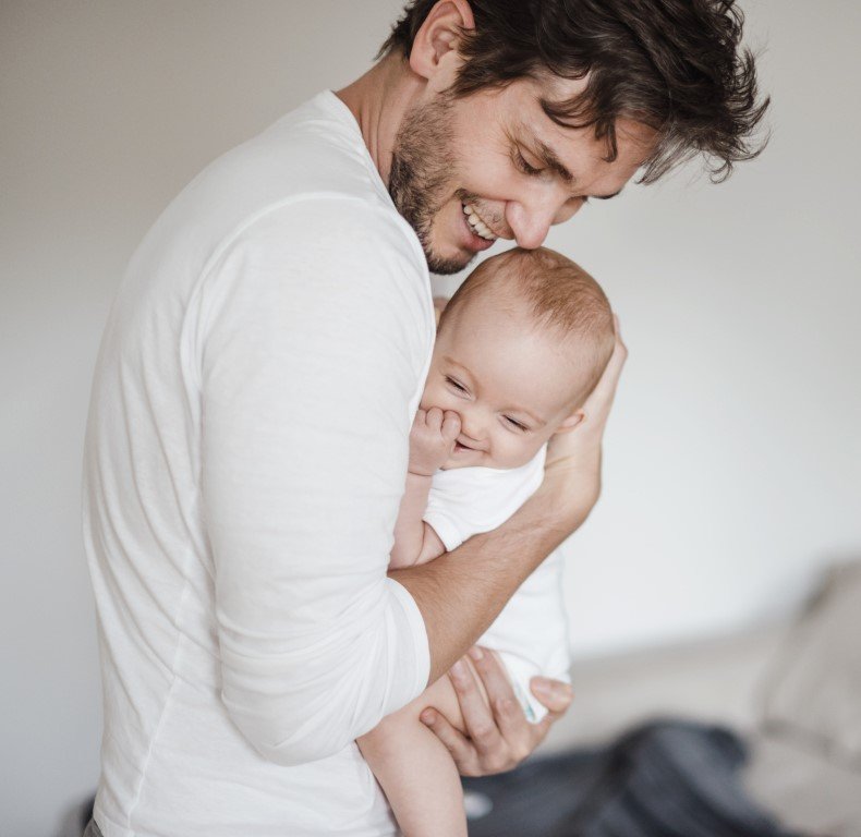 Ein junger Mann, der sanft ein fröhliches Baby im Arm hält.